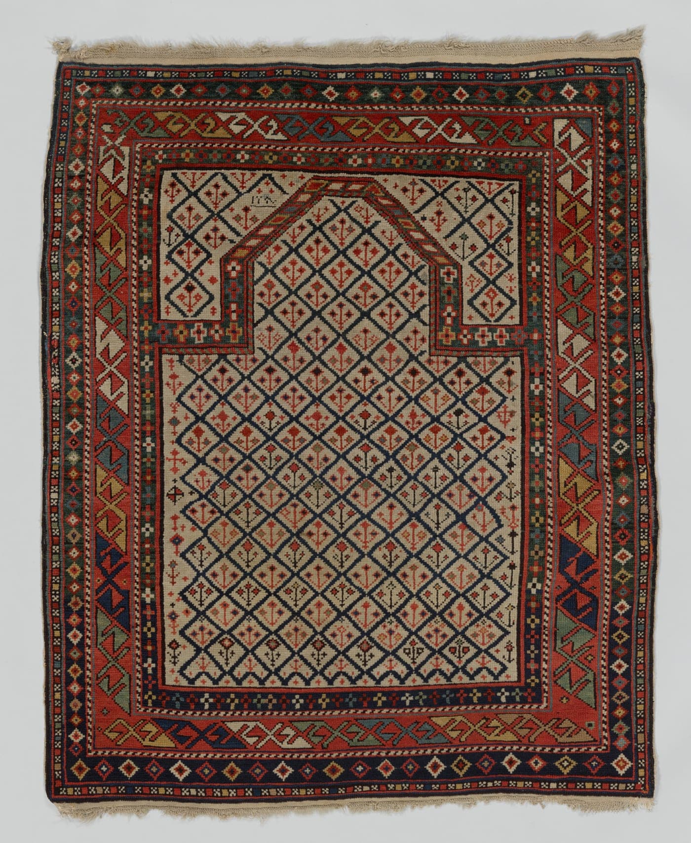 A small prayer rug with a pointed arch enclosing a lattice of small stylised flowers, each in a different colour, on an ivory ground.