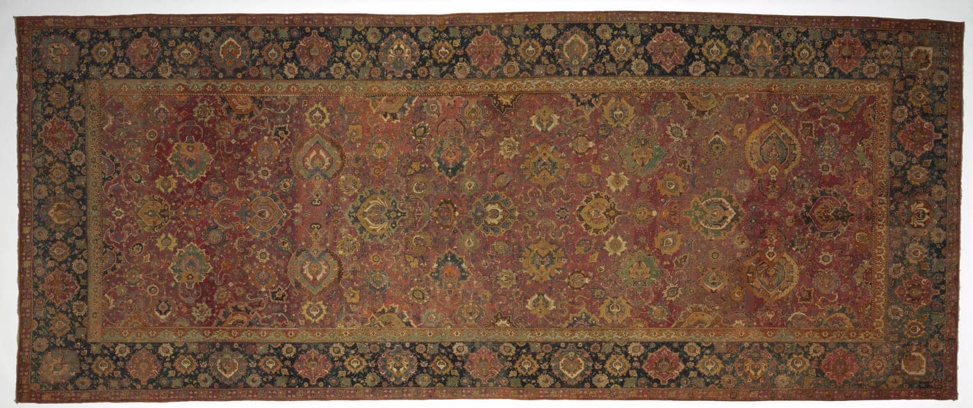 A fragment of a 16th-century carpet in deep blue and red, carrying a dense repeating field of rosettes framed by curving leaf forms.