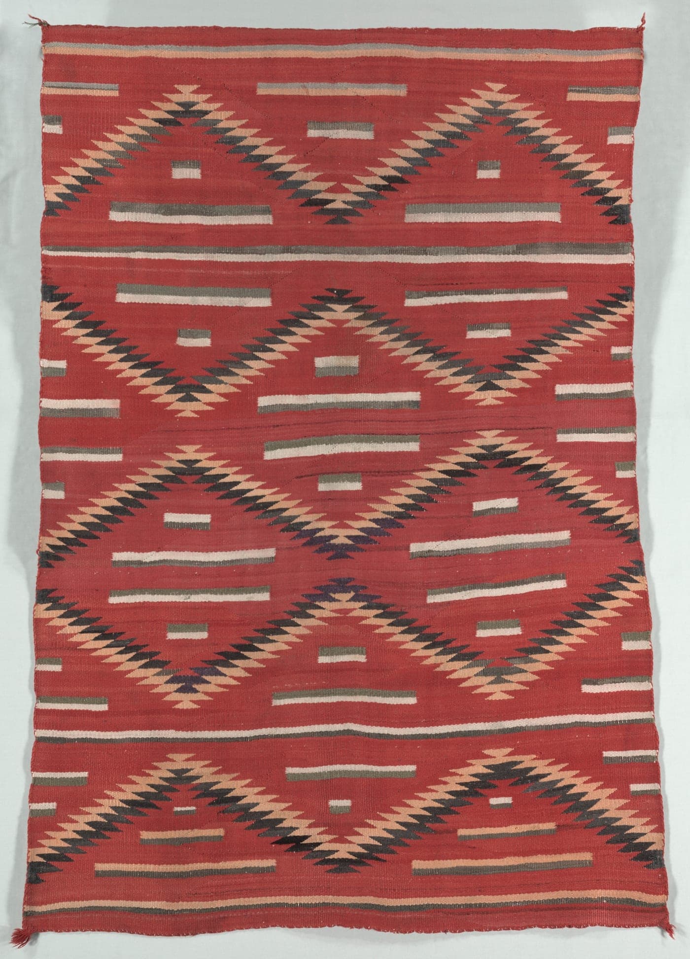 A densely patterned Diné rug in saturated red, orange, green and purple, built from serrated diamonds and zigzags that vibrate against each other.