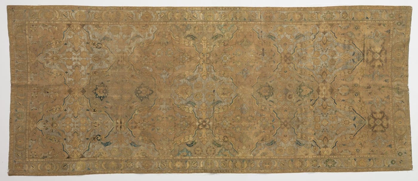 A 17th-century carpet in pale silk and metal thread, the colours softened almost to pastel, with a scrolling field design.