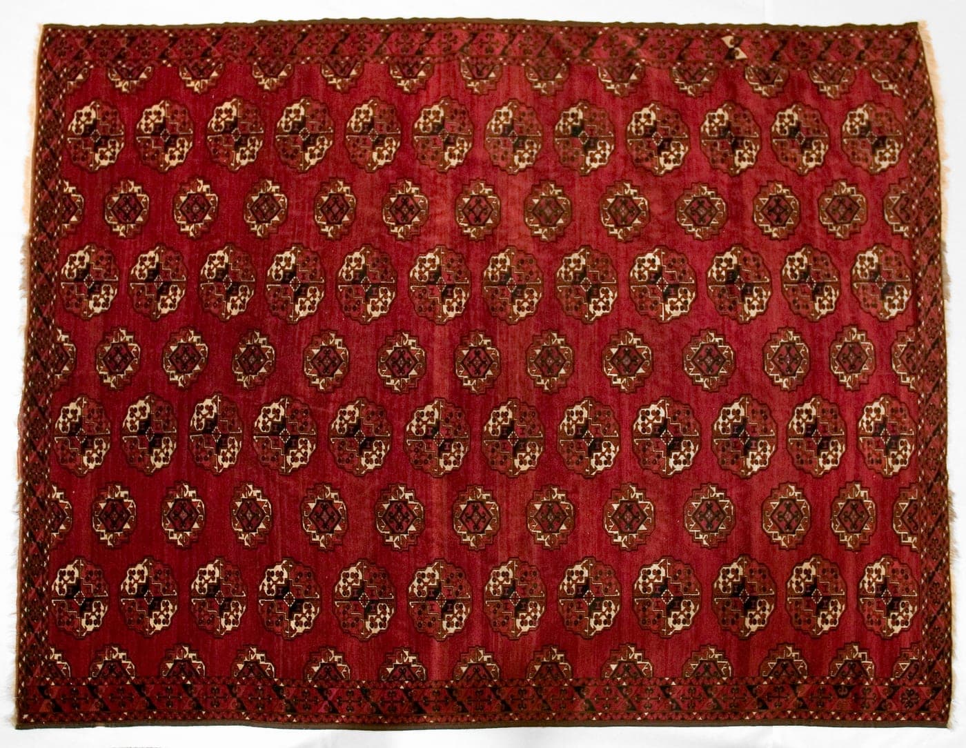 A dense Turkmen carpet in dark red and aubergine with rows of quartered guls, silk highlights catching the light in the small details.