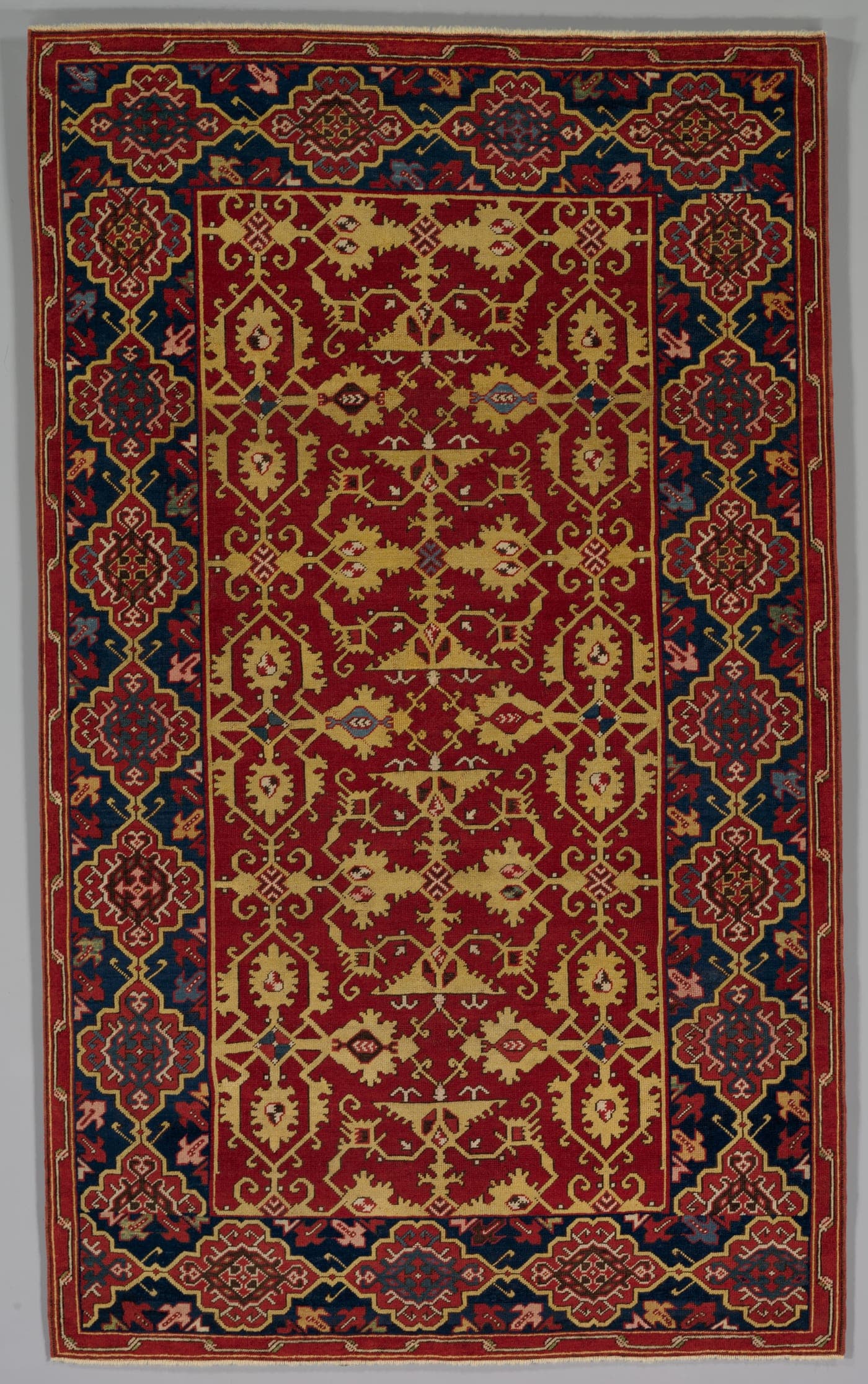 An Ottoman Ushak carpet with a red ground carrying an angular yellow lattice of stylised arabesques, framed by a border of stylised Kufic script.