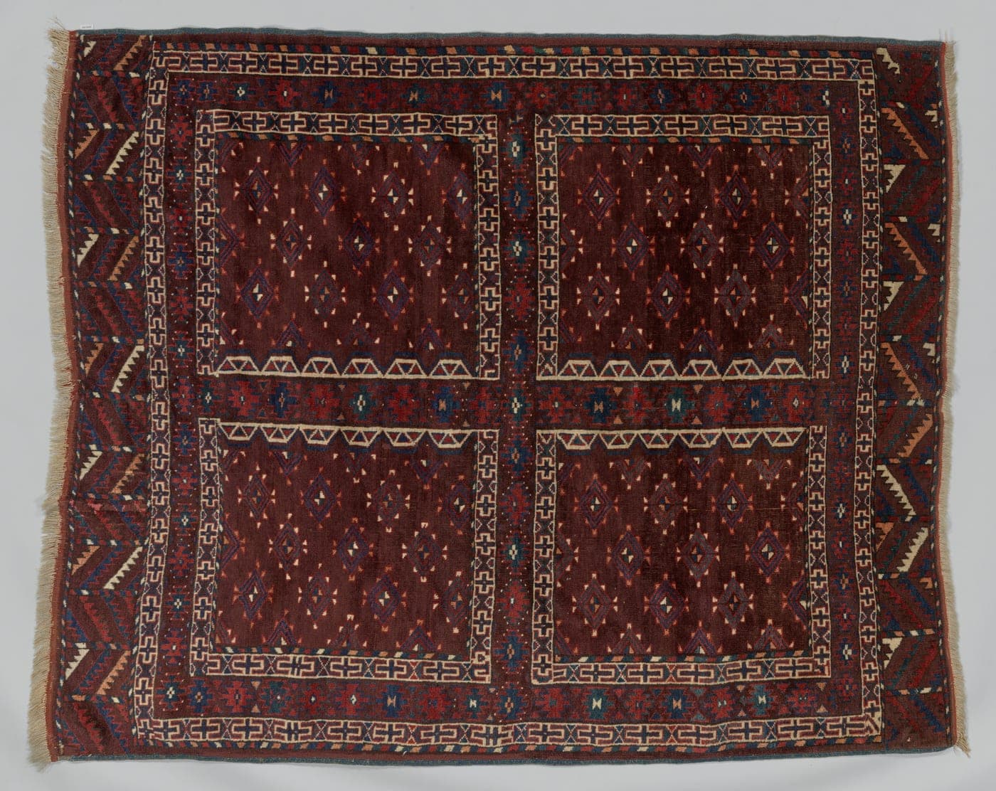 A Turkmen door rug divided into four panels by a broad cross, with a band of small stylised forms along the lower edge.