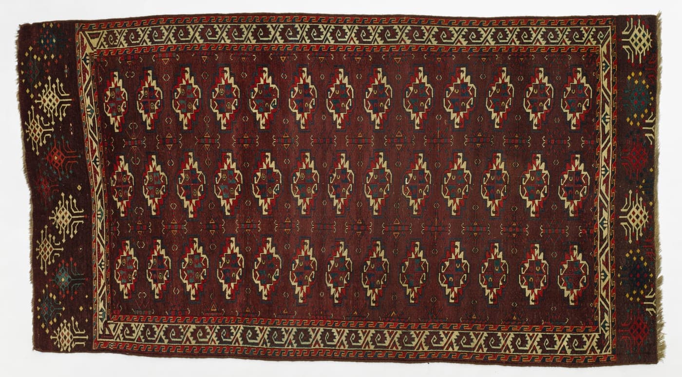 A Turkmen main carpet with a deep red-brown ground carrying rows of angular octagonal medallions in a strict lattice, with narrow patterned borders.